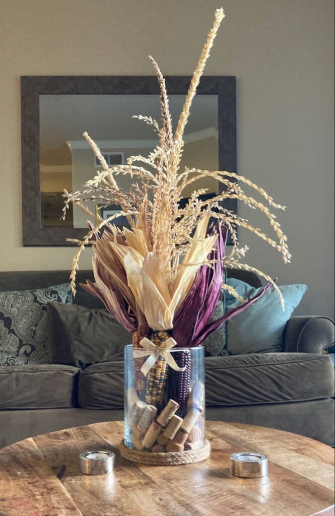 Elevate your decor with a captivating vase showcasing dried corn and an assortment of plants, evoking the beauty of the harvest season.