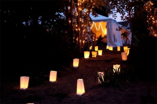 Discover the enchantment of a candle-lit path, leading to a cozy tent nestled in the shadows, creating a magical ambiance.